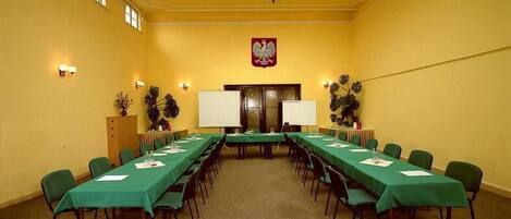 Una sala de conferencias con una larga mesa, sillas, una pizarra y un escudo en la pared.