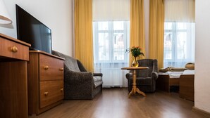 A modern living room with a flat-screen TV, wooden furniture, a small round table with a vase, and large windows with yellow curtains. - Hotel EUROPA (Jelenia Gora)