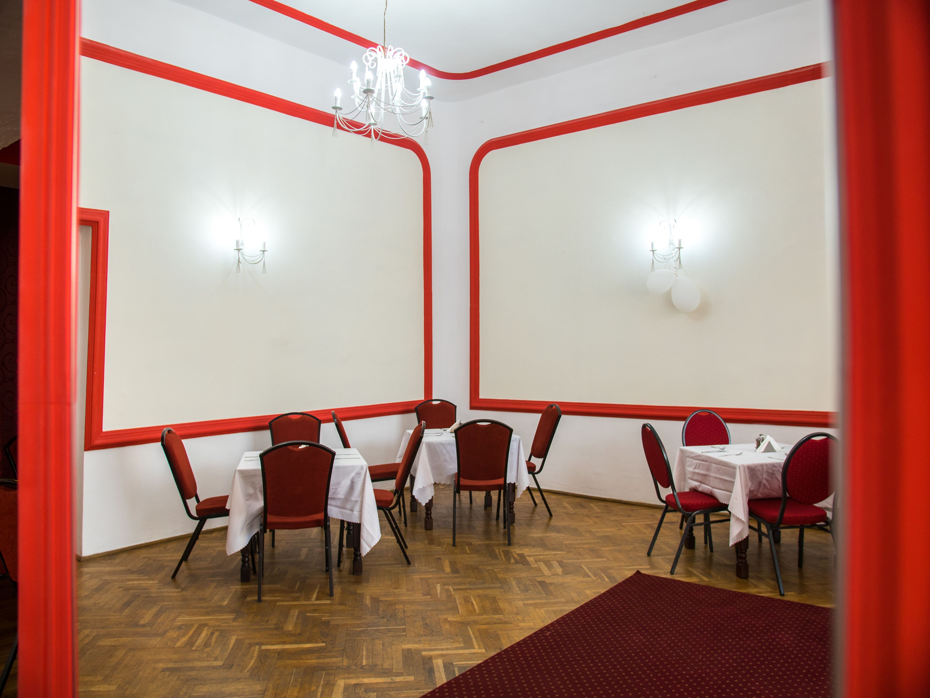 Un espace repas décoré de rouge et de blanc, doté d’un plancher en bois et de tables dressées pour le service.