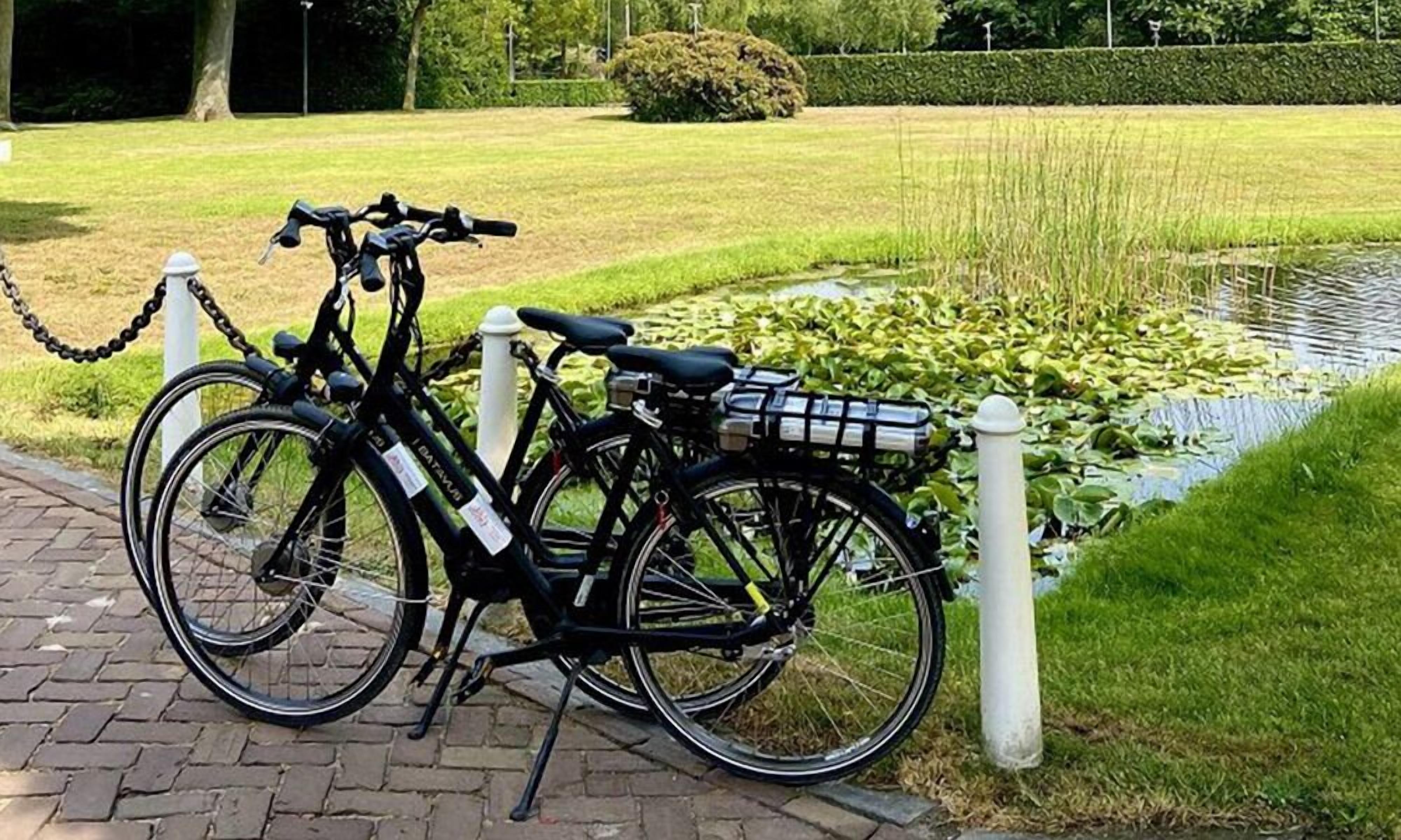 A bicycle parked by a paved path next to a pond with lily pads.