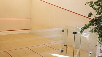 Pista de squash amb barreres de vidre, paviment de fusta i línies vermelles que marquen el camp.