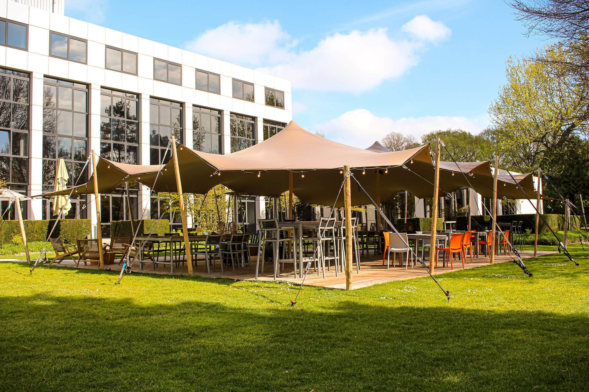 An outdoor seating area with tables and chairs, surrounded by a grassy lawn, and a modern building in the background.