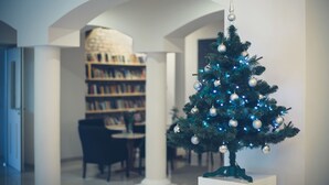 A small decorated Christmas tree in a room with a bookshelf and a dining area. - Hotel Impresja (Duszniki Zdroj)