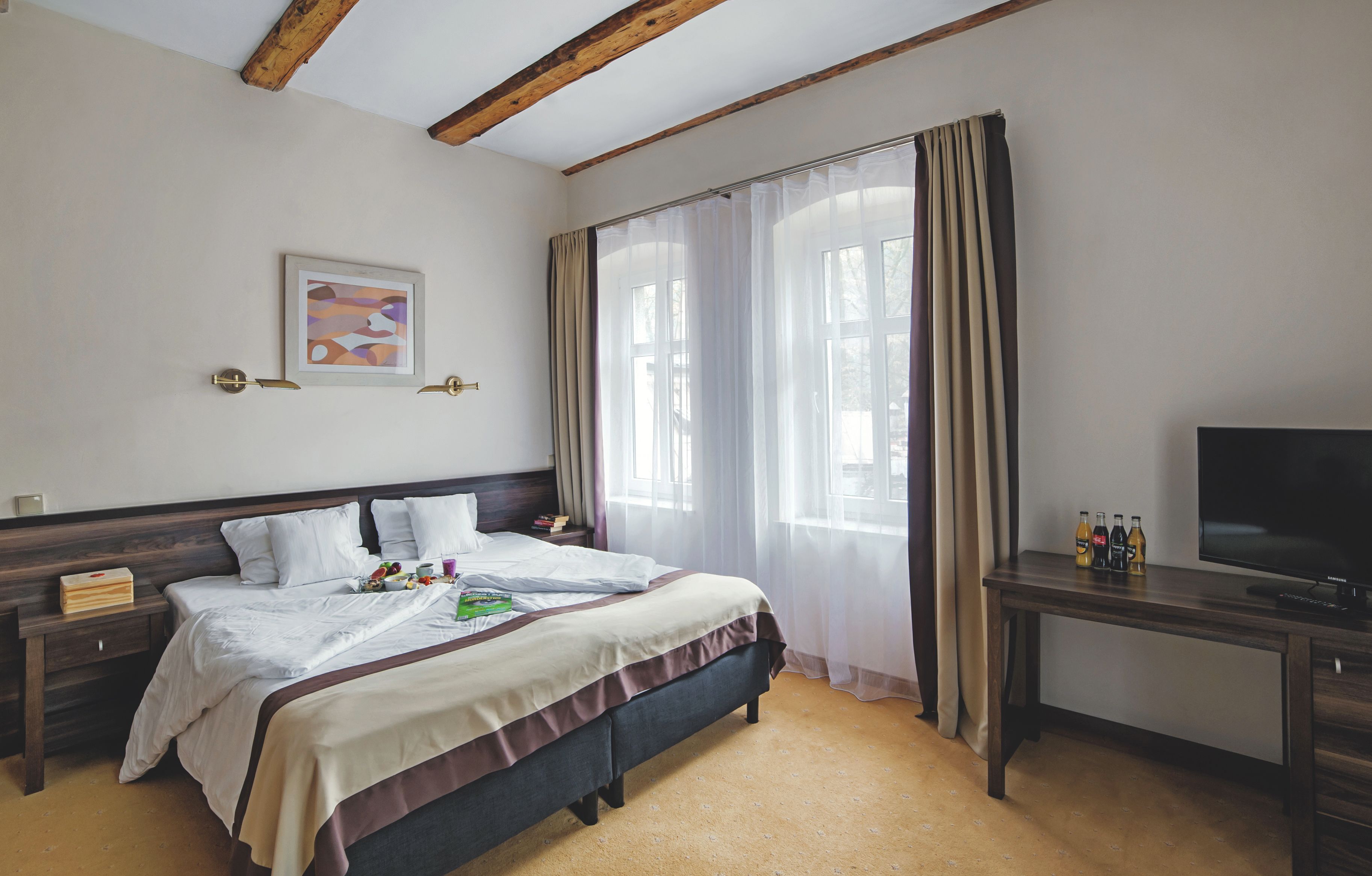 A hotel room with a bed, a desk, a TV, and a window with curtains.
