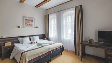 A hotel room with a bed, a desk, a TV, and a window with curtains.