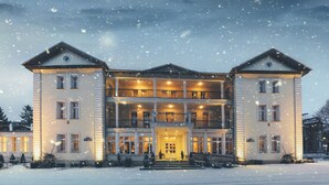 A large, two-story building with a central entrance and multiple balconies, surrounded by snow. - Hotel Impresja (Duszniki Zdroj)