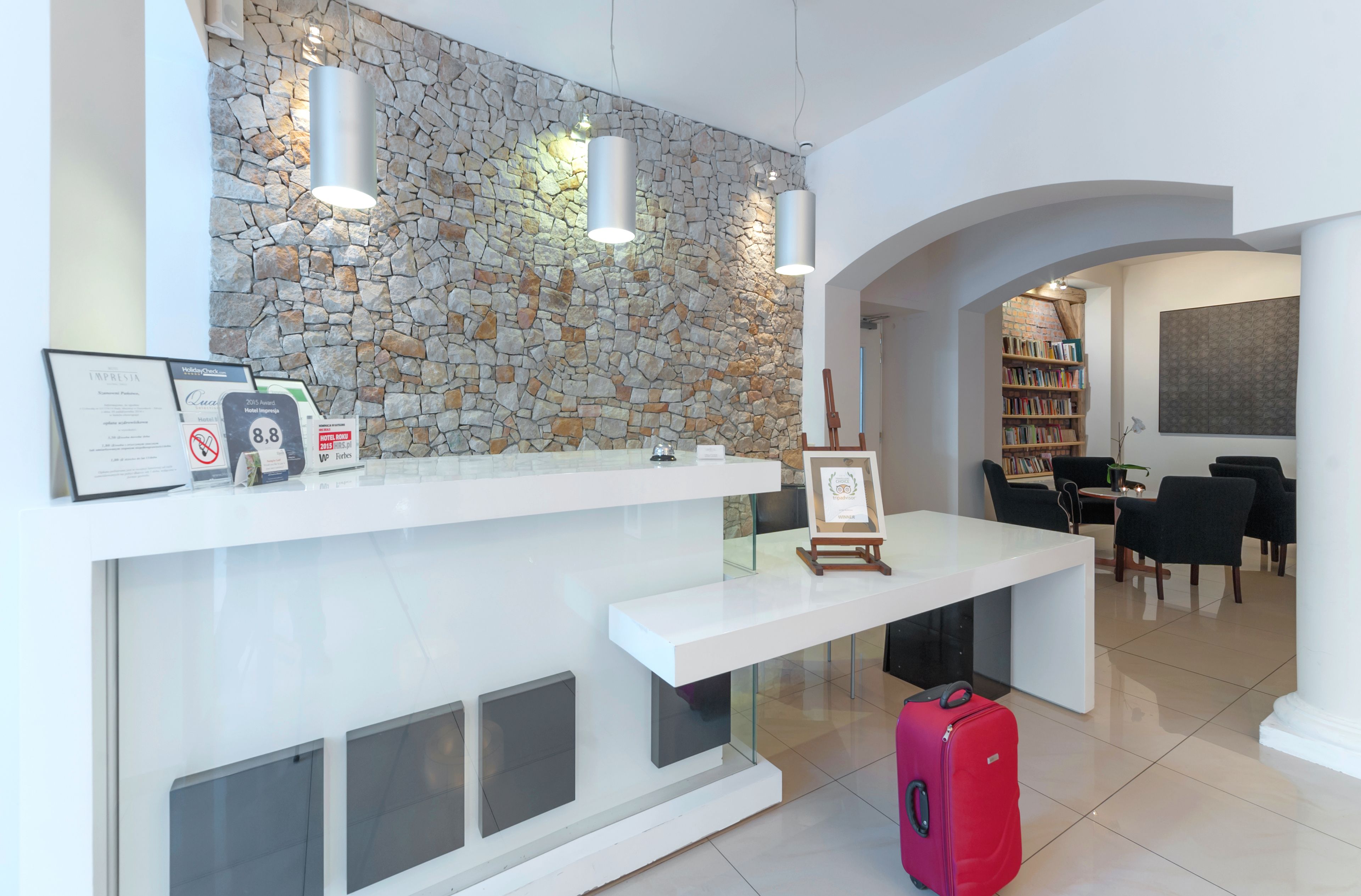 A reception area with a stone wall, a white reception desk, a red suitcase, and a bookshelf in the background.
