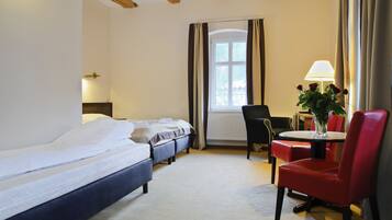 A hotel room with a large bed, two smaller beds, a dining table with chairs, and a window with curtains.