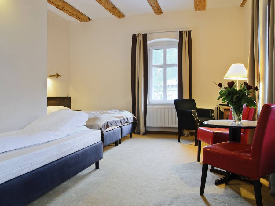 A hotel room with a large bed, two smaller beds, a dining table with chairs, and a window with curtains.