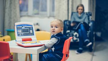 Un niño usando una tableta en una mesa, en una habitación con ventana y una silla al fondo.