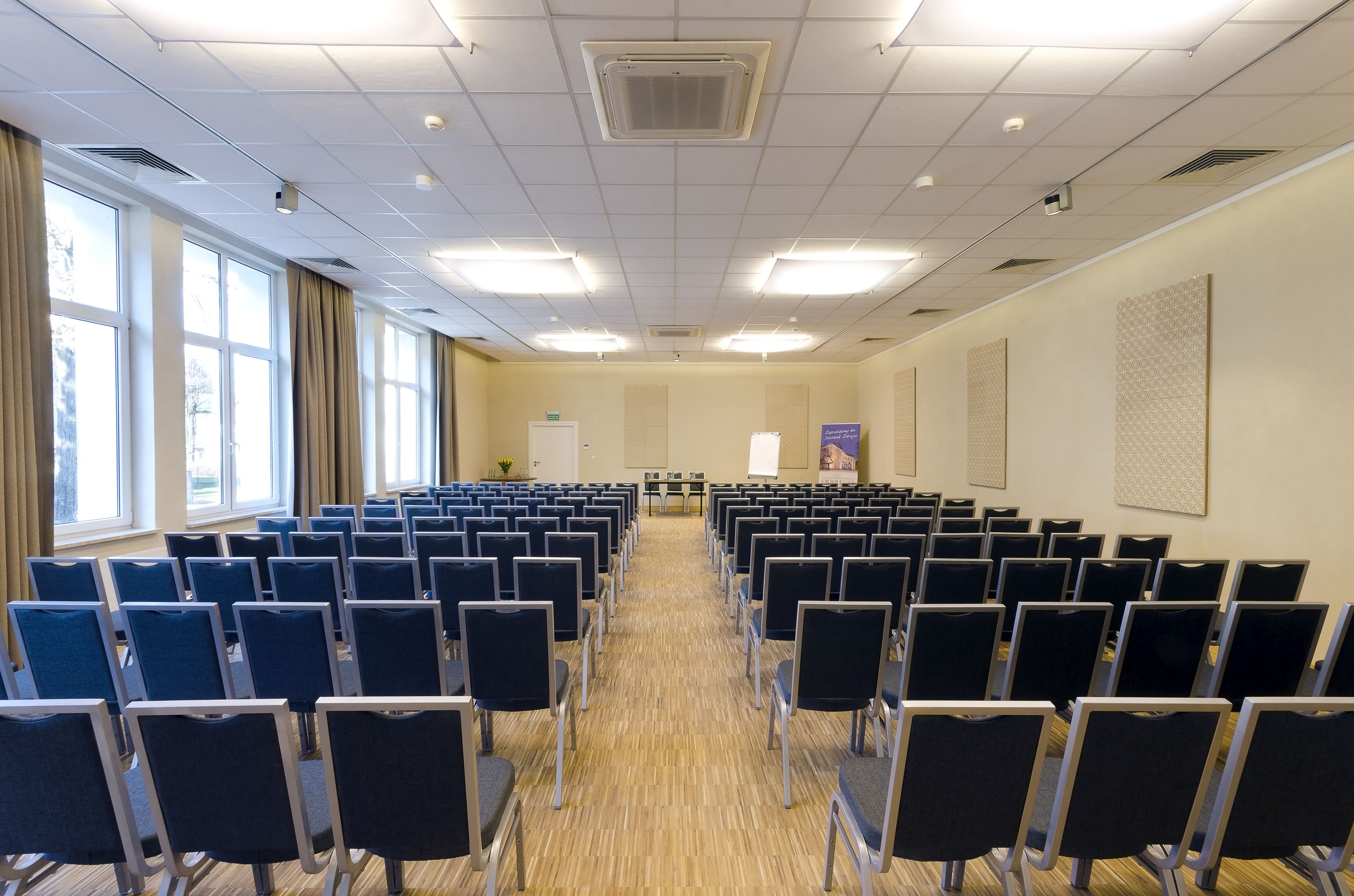 Ein Konferenzraum mit Reihen von Stühlen, großen Fenstern und einer Tafel an der Wand.