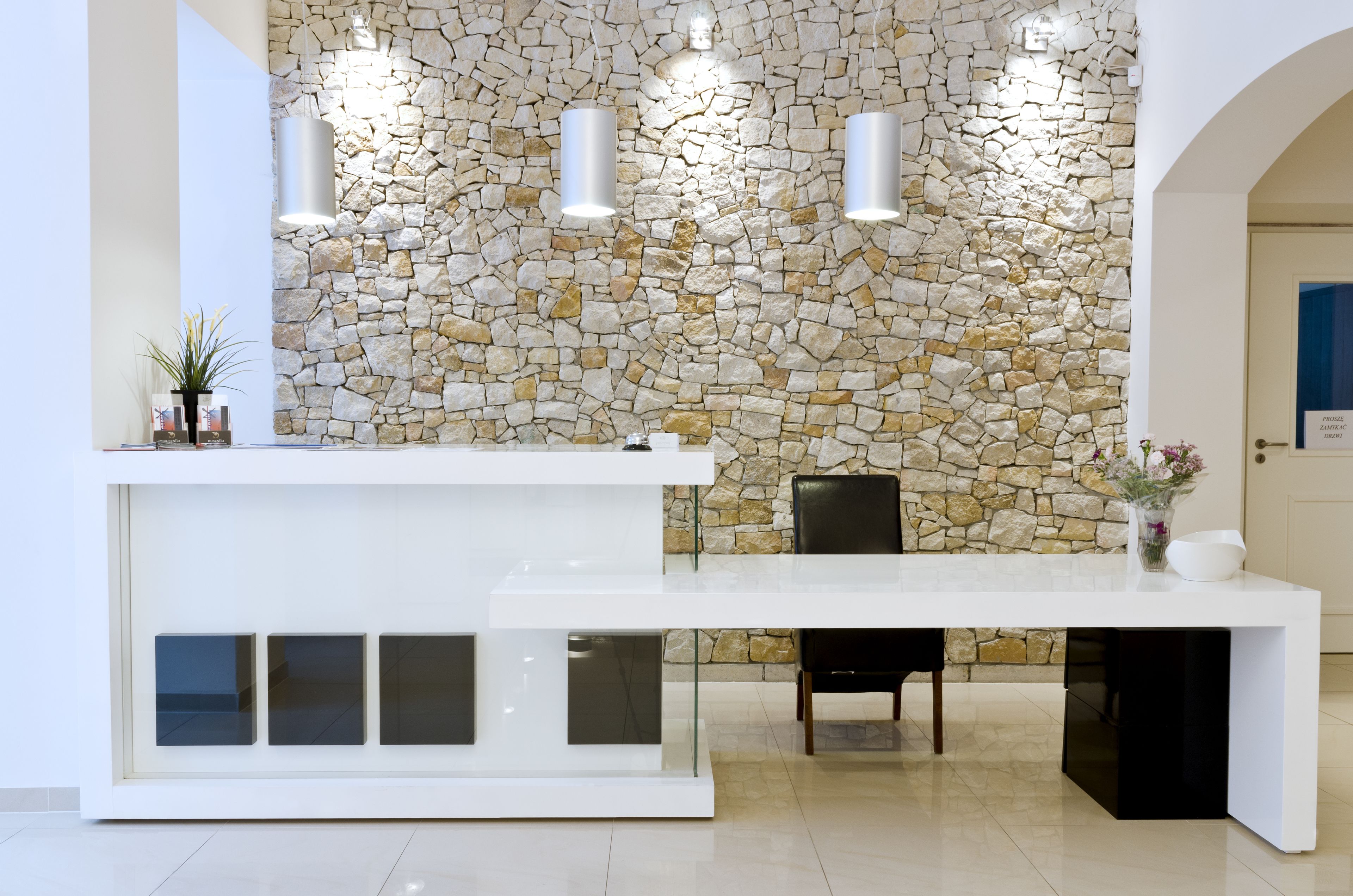 A reception desk with a stone wall backdrop, a black chair, and a vase with flowers.