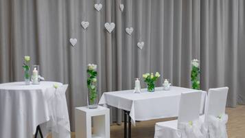 Een kamer met twee tafels, elk gedekt met een witte tafelkleed en een kaars, versierd met witte rozen en hartjes.
