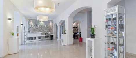 A spacious lobby with a central reception desk, a modern kitchen area, and a glass display case with items.