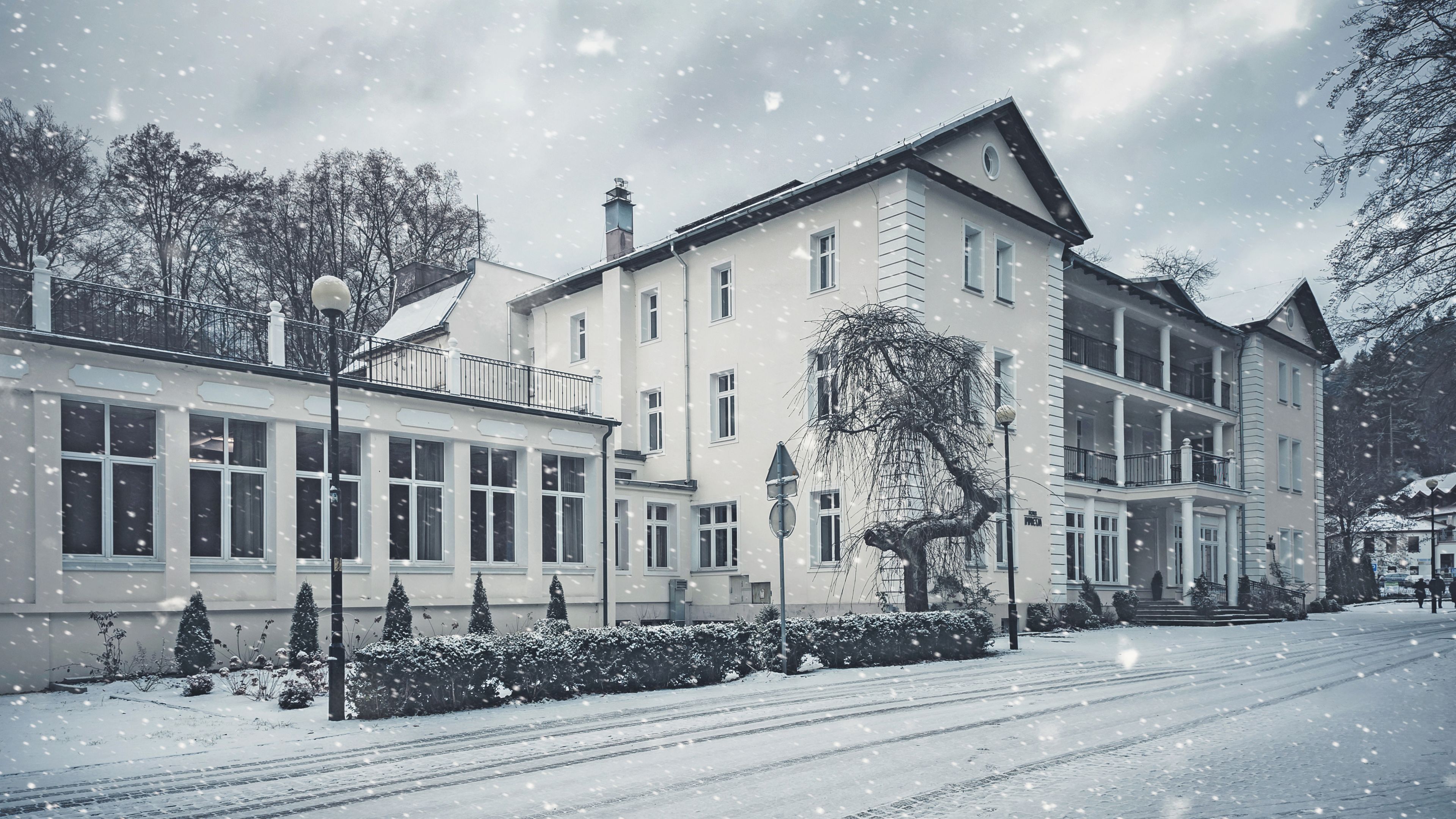 A multi-story building with large windows and a balcony, surrounded by snow-covered trees and a snow-covered street.