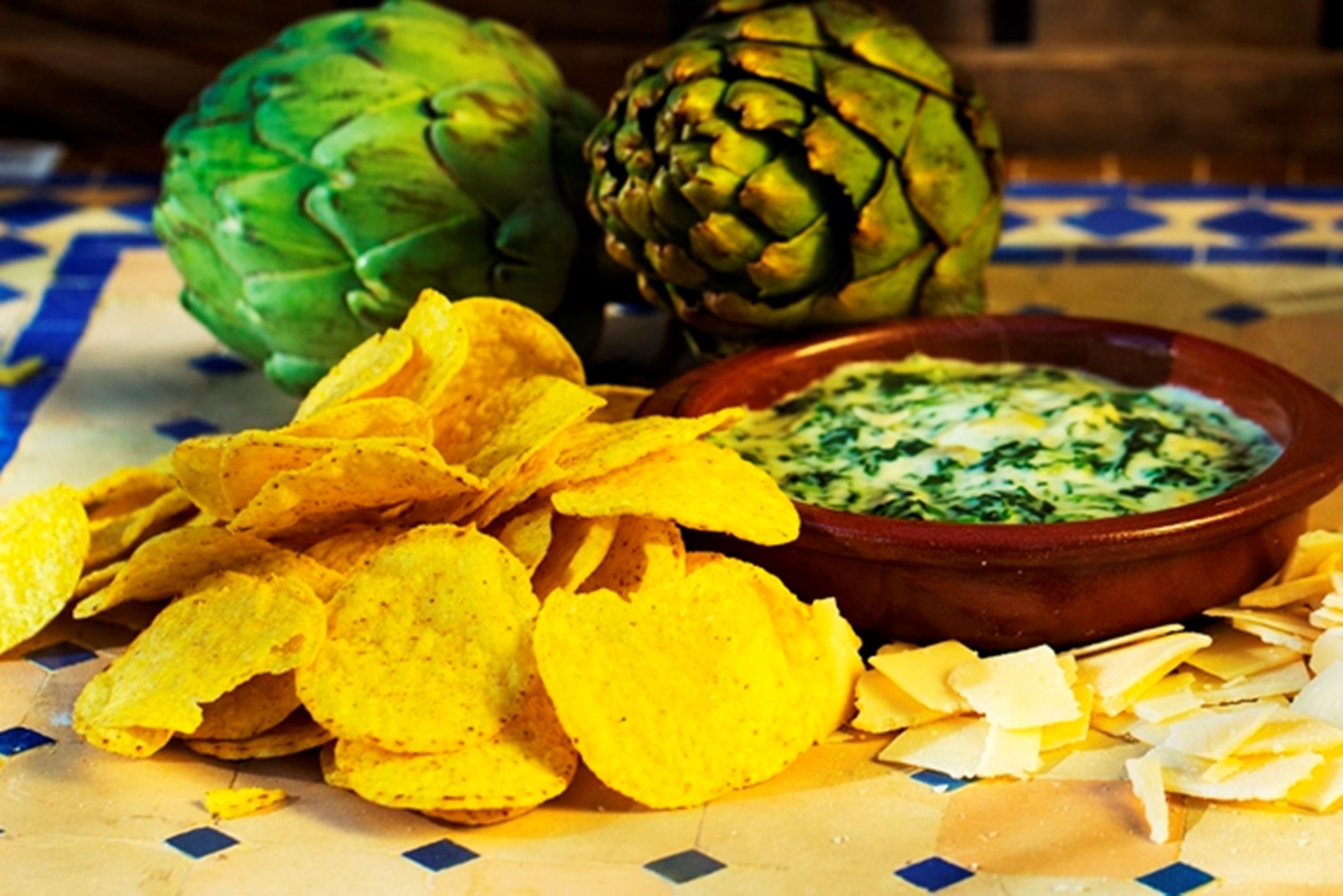Een tafel met artisjokhartjes, tortilla chips en een bakje dip.