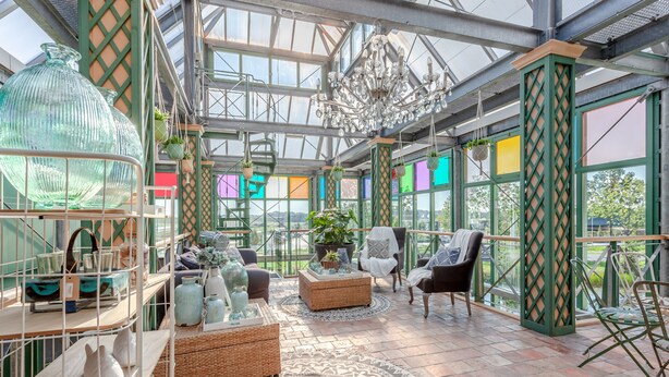 A conservatory with a glass ceiling, wicker furniture, and a chandelier. - HarTeluk Joure (Joure)