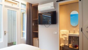 A hotel room with a bed, a television mounted on the wall, a bathroom with a sink and mirror, and an air conditioning unit. - HarTeluk Joure (Joure)