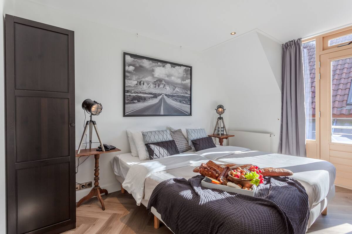 A bedroom with a large bed, a desk, a tripod, and a framed picture on the wall.