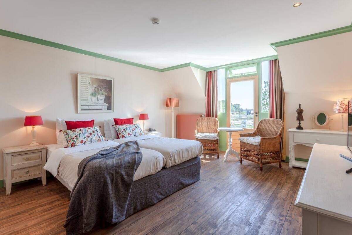 A hotel room with a bed, two bedside tables with lamps, a chair, a desk, and a window with curtains.
