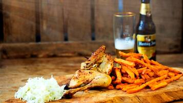 Een houten tafel met een gebraden kippenschenkel, een glas bier en een hoop friet.