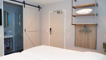 Moderni hotellihuone, jossa on suuri sänky, liukuovi kylpyhuoneeseen, puinen hylly, jossa on tilaa vaatteille, ja pieni yöpöytä.