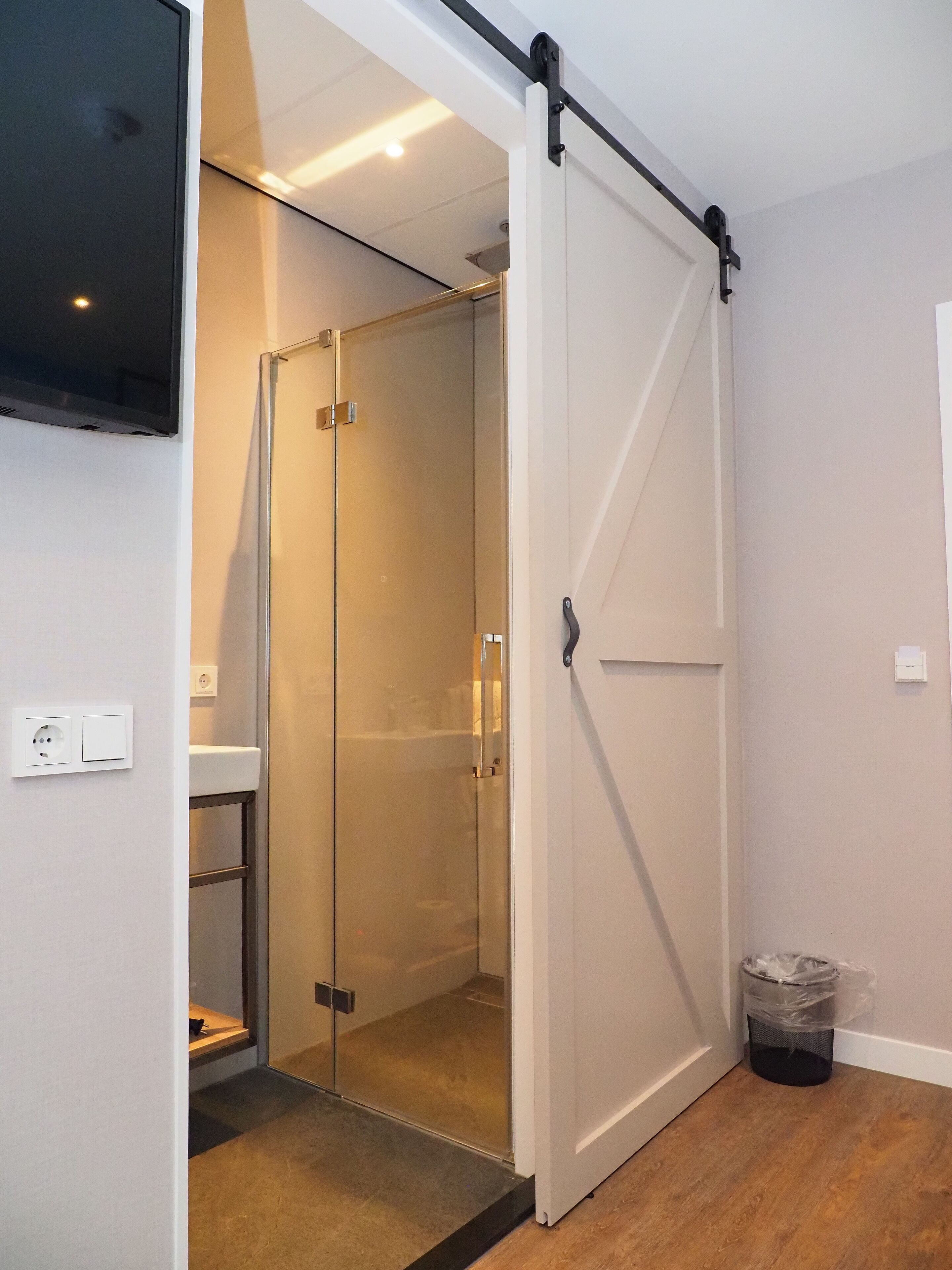 Une salle de bain moderne avec une douche à parois de verre, une porte blanche et un téléviseur fixé au mur.