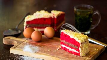 Una rebanada de pastel de terciopelo rojo sobre una tabla de madera con huevos y un recipiente de azúcar cerca.