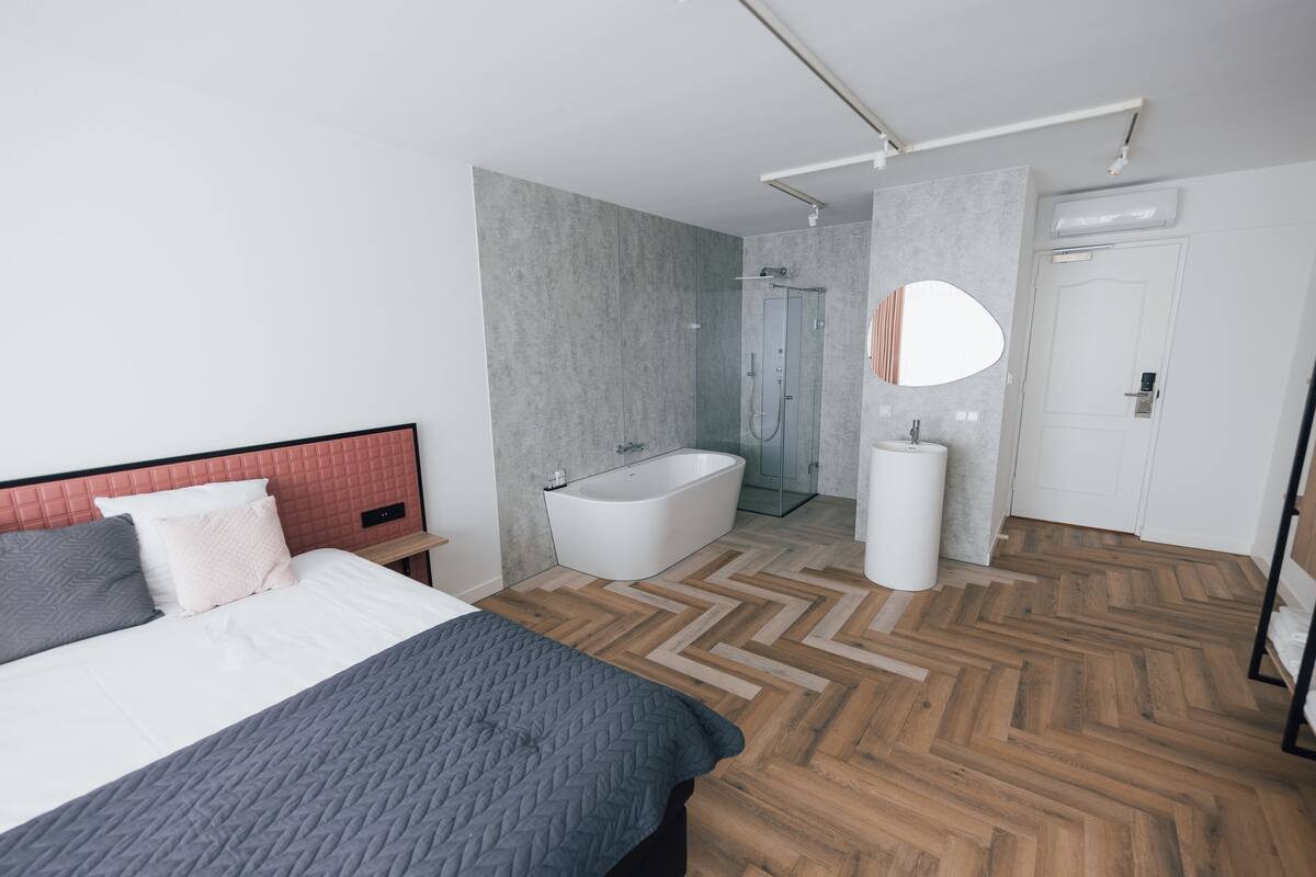 A modern bedroom with a large bed, a walk-in closet, and a bathroom with a bathtub and shower.