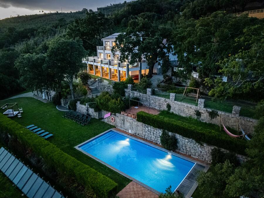 A modern house with a swimming pool, surrounded by well-maintained gardens and a stone wall.