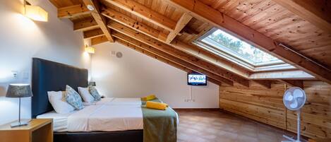 A bedroom with a sloped ceiling, a bed, a nightstand, a lamp, a TV, and a fan.