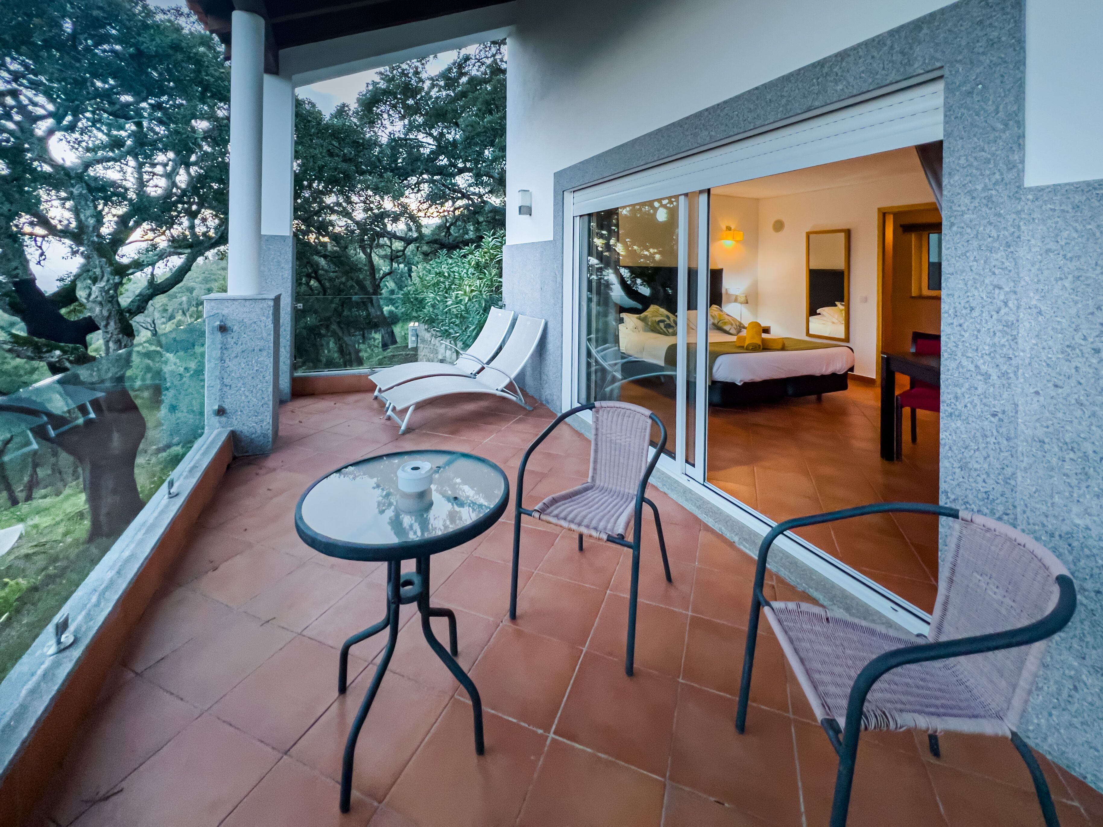 A balcony with a glass door leading to a bedroom. There are two lounge chairs and a small table.