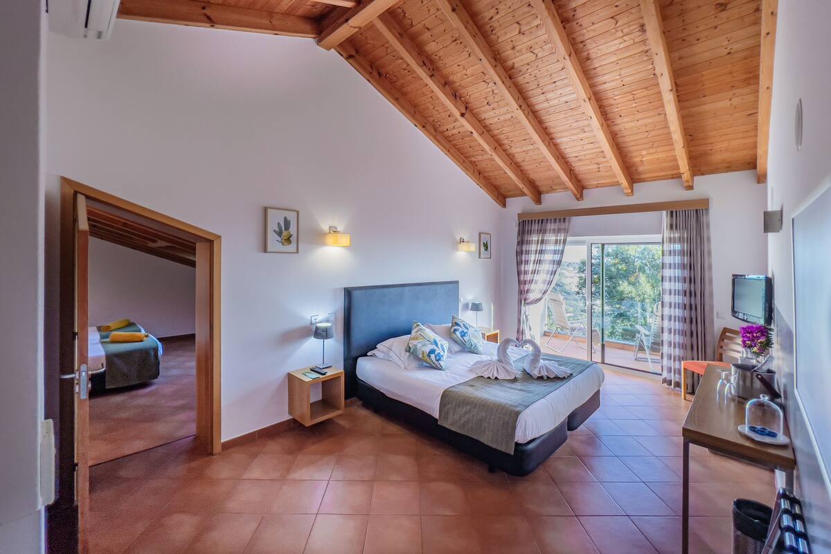 A bedroom with a bed, bedside tables, a TV, and a balcony with a view.