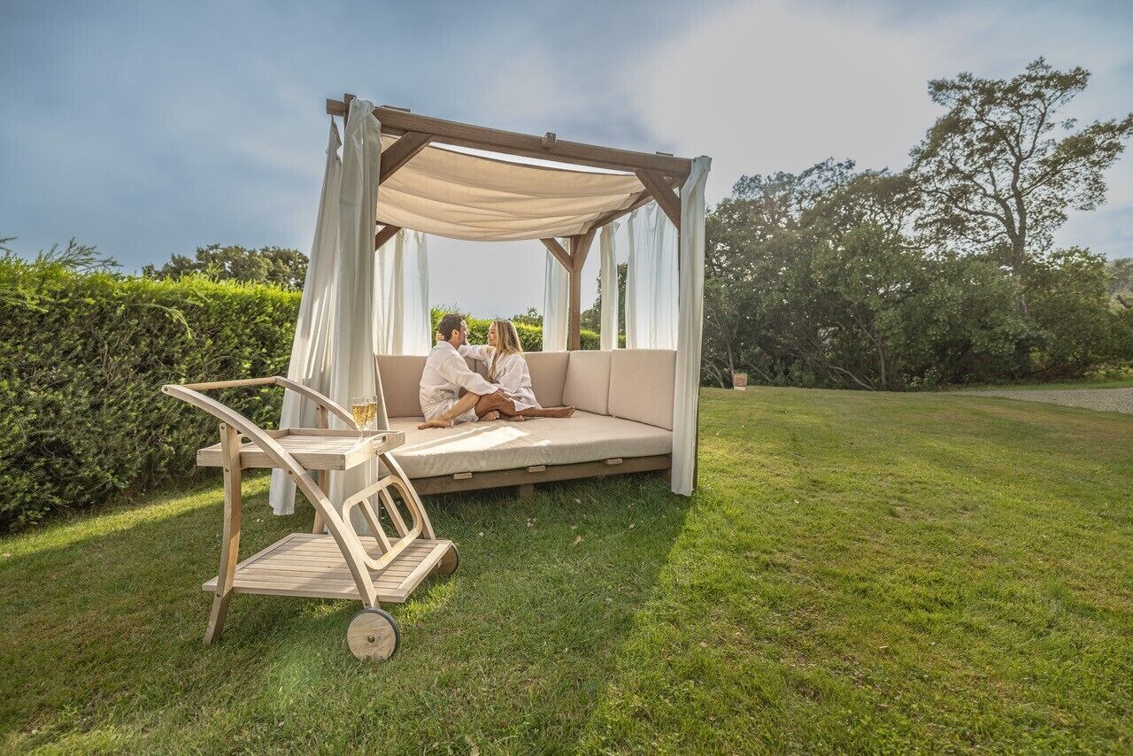 A wooden gazebo with a canopy, a cushioned bench, and a small wooden table.