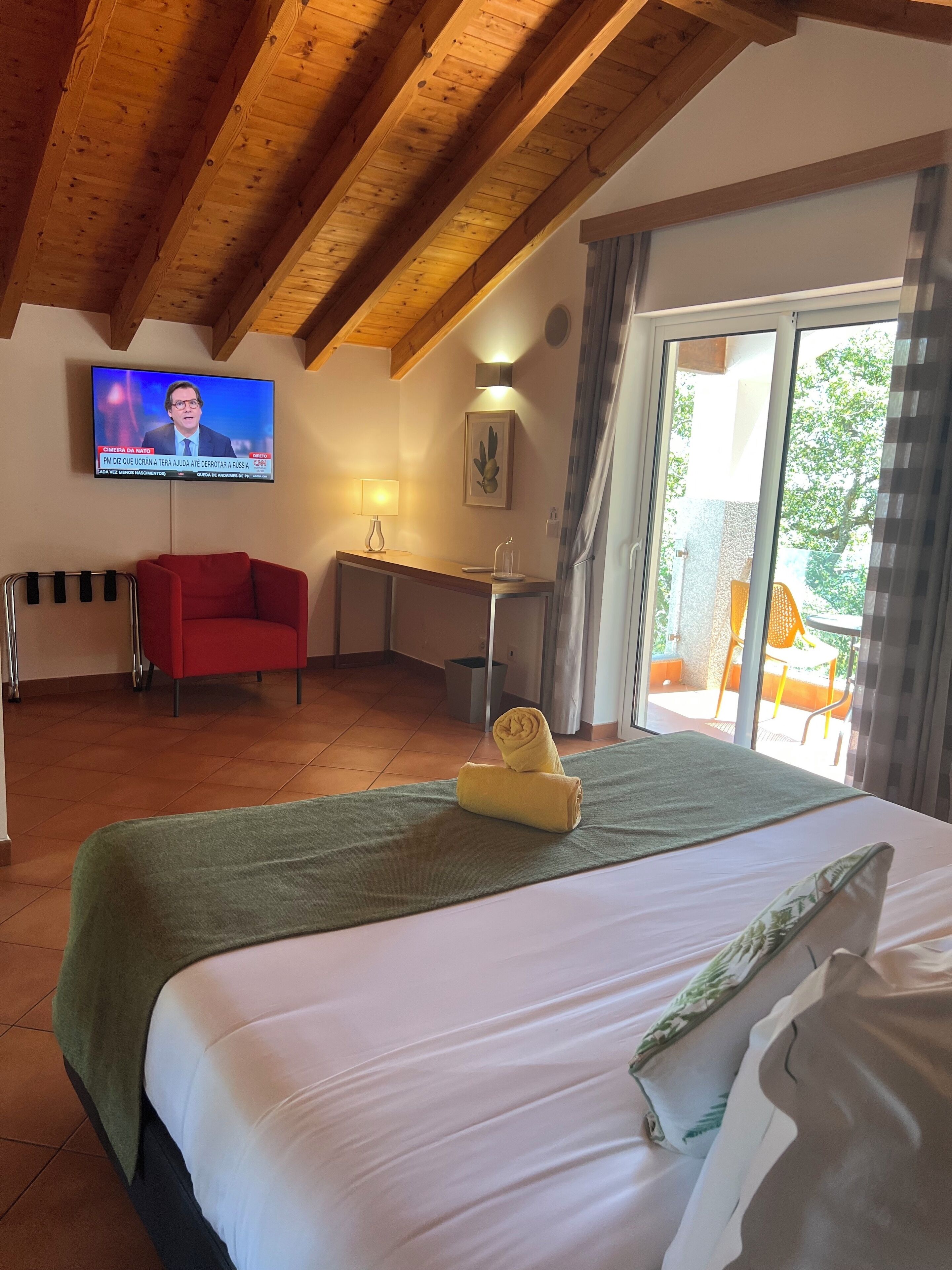 A hotel room with a bed, a TV mounted on the wall, a desk, and a chair.