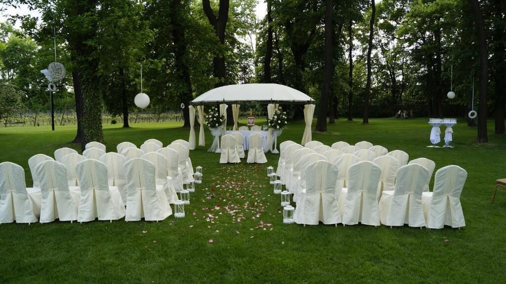 An outdoor wedding ceremony with white chairs arranged in rows, a canopy, and a floral arrangement at the front.