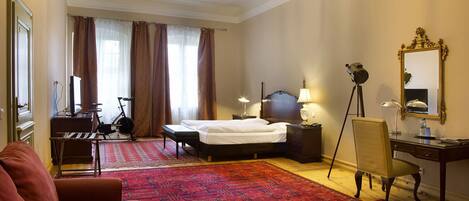 A hotel room with a bed, a desk with a chair, a television, a bicycle, and a large red carpet.
