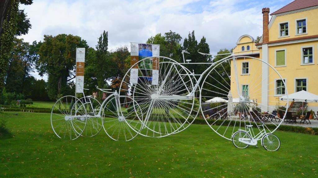 A large white bicycle sculpture in a park with a building in the background.
