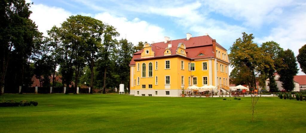 A large, yellow building with a red roof, surrounded by a well-maintained lawn and trees.