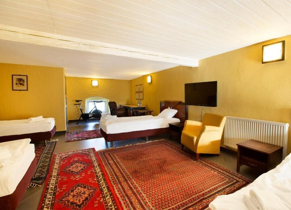 A hotel room with two single beds, a sofa, a chair, a TV, and a radiator.