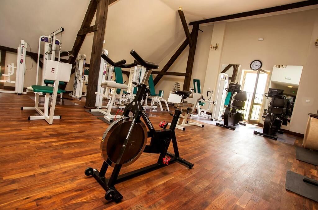 Ein Fitnessraum mit verschiedenen Trainingsgeräten, Holzdielen und freiliegenden Balken.
