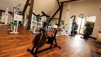 Ein Fitnessraum mit verschiedenen Trainingsgeräten, Holzdielen und freiliegenden Balken.