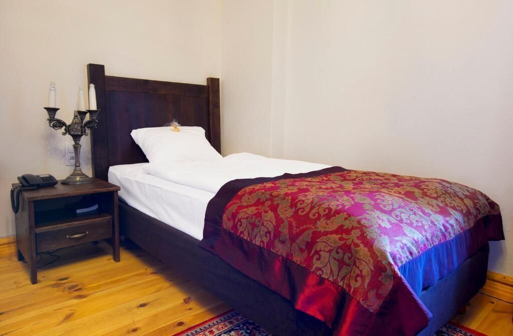 A single bed with a wooden headboard, a bedside table with a lamp, and a patterned throw blanket.