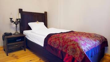 A single bed with a wooden headboard, a bedside table with a lamp, and a patterned throw blanket.