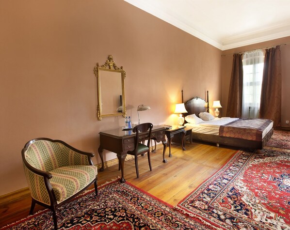 Une chambre d’hôtel avec un lit, un bureau et une chaise, un grand miroir et un sol recouvert de moquette.