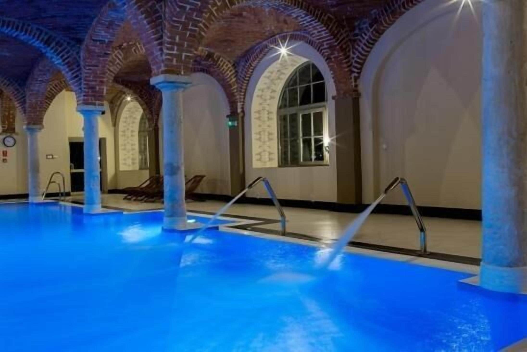 Una piscina interior con iluminación azul, arcos de ladrillo y una vista despejada del área de la piscina.