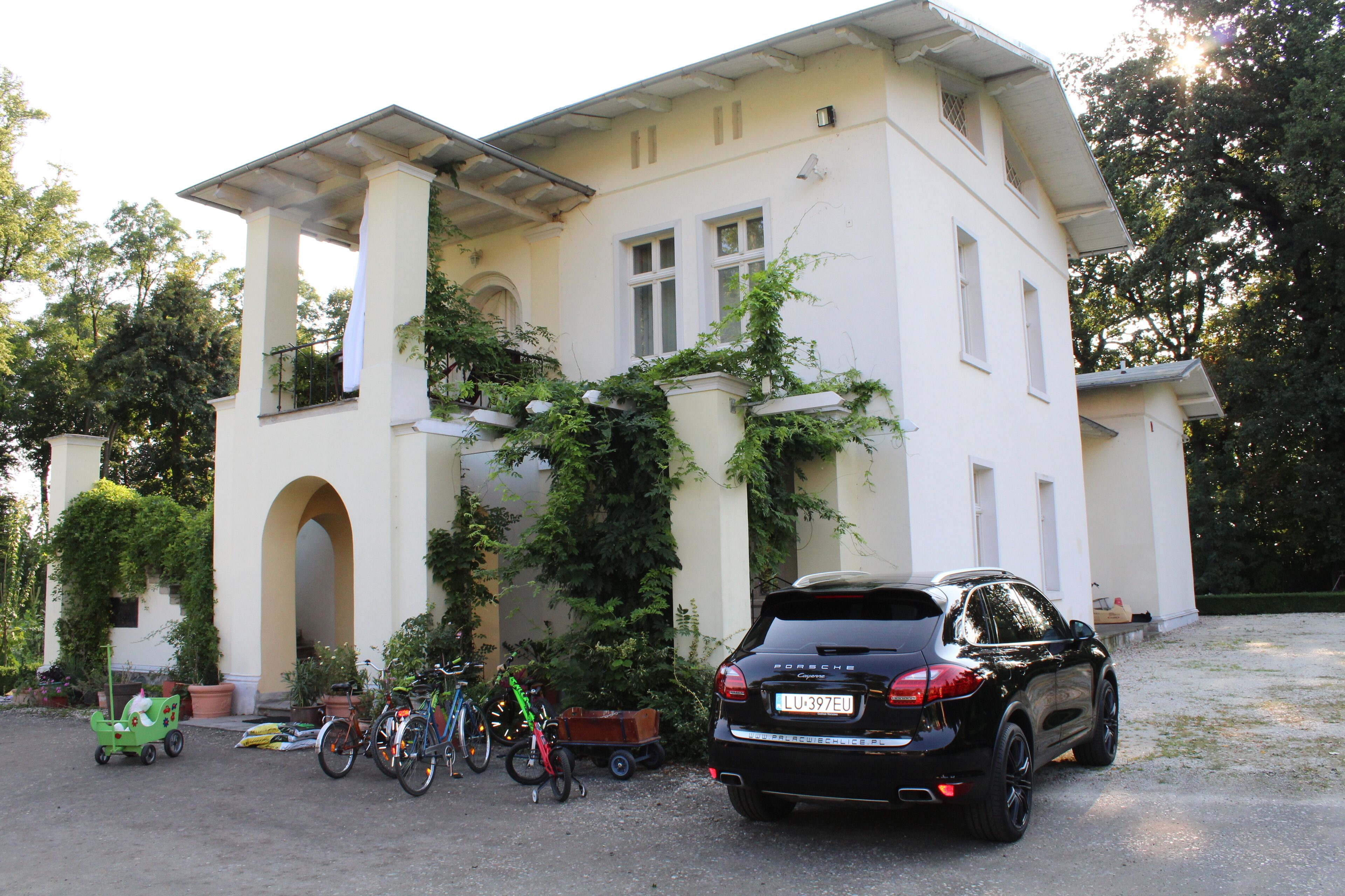 Una casa de dos pisos con fachada blanca, un porche cubierto y un automóvil negro estacionado.