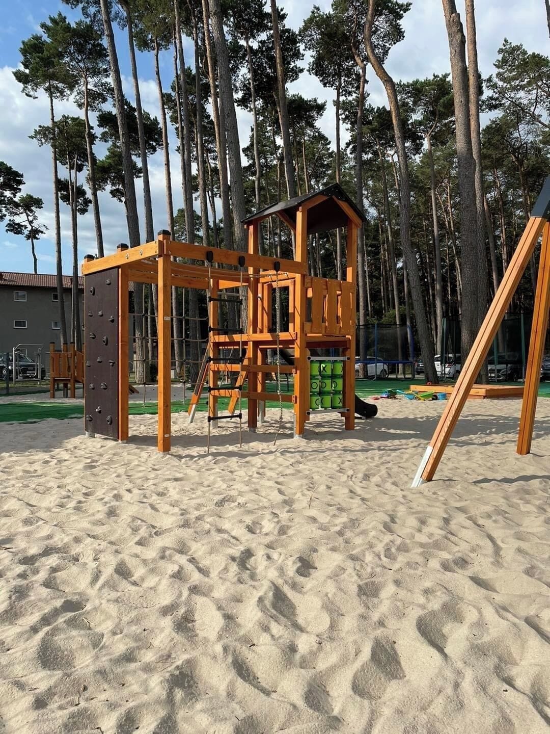 En lekställning av trä på en sandstrand, med höga träd i bakgrunden.