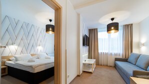 Quarto de hotel com cama, sofá, televisão e uma pequena mesa.