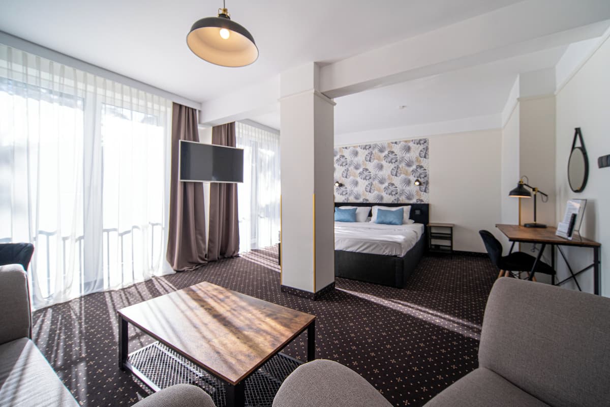 A hotel room with a bed, a desk, a TV, and a seating area.